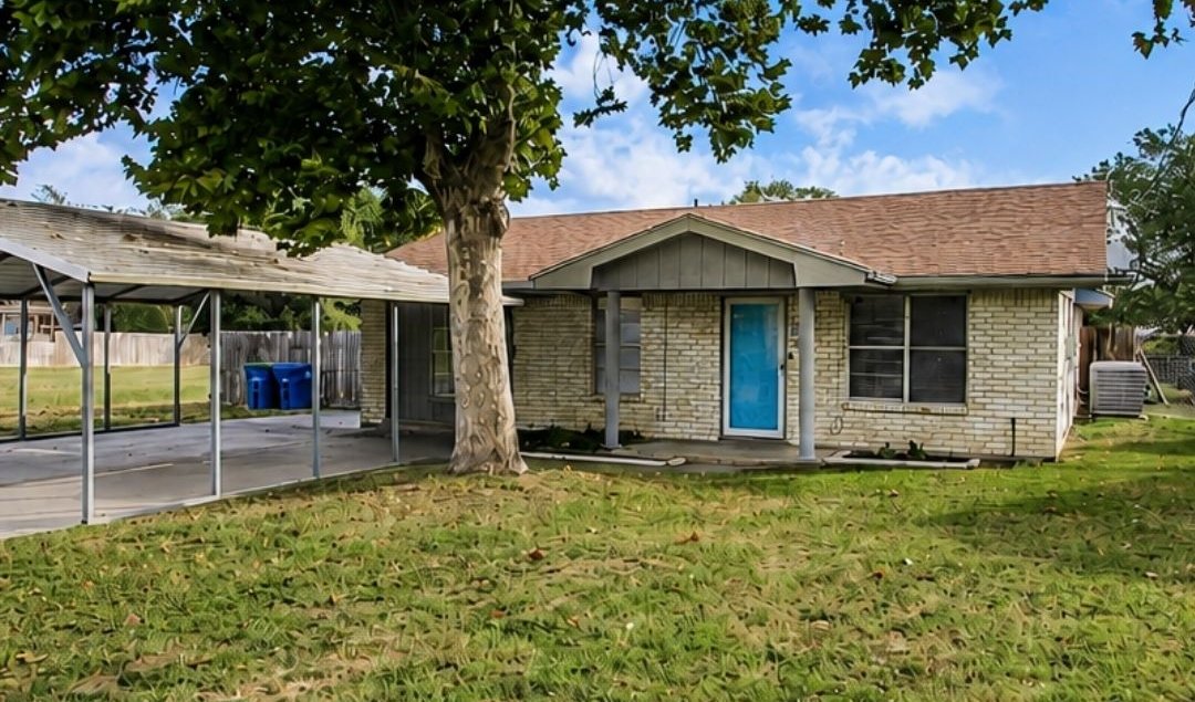 606 N. Berry St.: a one-story brick home with a bright blue front door, a big shade tree and a carport